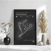 a poster of the Shanghai International Circuit, a racing circuit in Shanghai, China. The poster displays a map of the circuit and includes various details about the circuit, such as its location, size, and the number of turns. The poster is framed and placed on a white surface, with a vase of flowers and a potted plant to the left and a small white object to the right.