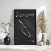 a black poster with a white outline of a race track, displaying the text "CIRCUIT GILLES VILLENUEVE" and "Montreal, Canada" along with various race statistics and locations. The poster is framed and placed on a white wall, with a vase of flowers and a potted plant to the left, and a small white object to the right.