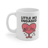 White ceramic mug with a cartoon heart character holding an engagement ring and the phrase “Little Ms Engaged” – a funny gift for a newly engaged bride-to-be.