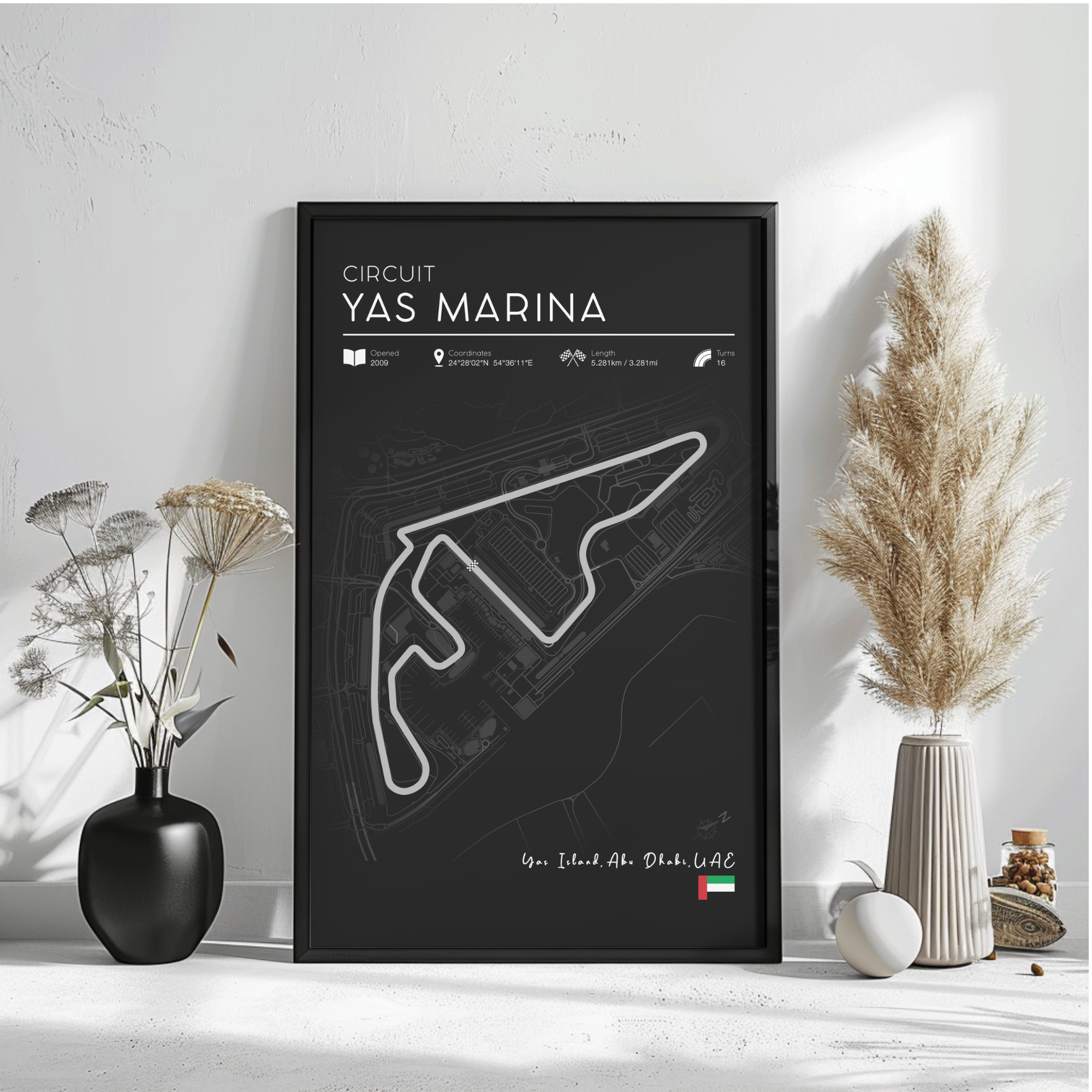 a poster of the Circuit Yas Marina, a racing circuit in Dubai, United Arab Emirates. The poster is displayed on a wall, with a vase of flowers and a potted plant to the left and a small white object to the right.