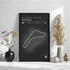 a poster of the Monza racetrack in Italy, with a black background and white text. The poster includes information about the track, such as its name, location, and features. The poster is displayed on a wall, with a vase of flowers and a potted plant to the left, and a small white object to the right.