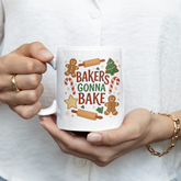 A person is holding a white mug with a colorful design featuring gingerbread men and the text "Bakers Gonna Bake".