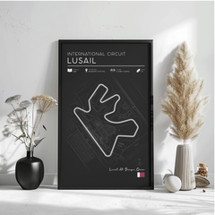 a poster of the International Circuit Lusail, a racing circuit located in Dagenham, Qatar. The poster is framed and displayed on a wall, with a vase of flowers and a potted plant to the left and a small white object to the right.
