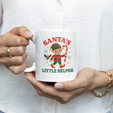 Person holding a mug with a 'Santa's Little Helper' design featuring an elf.