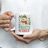 Person holding a mug with a snowman design and 'Frosty Vibes' text.