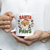 Person holding a mug with 'Santa Paws' design featuring a dog wearing a Santa hat.